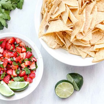 image is a bowl of Strawberry salsa with 2 lime wedges. www.atwistedplate.com/strawberry-salsa/